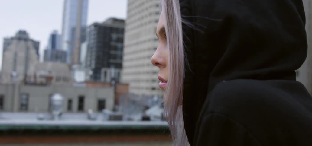 A young woman looks out at a city from the rooftop of a building during the day