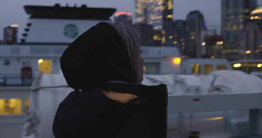 Young woman wearing a hoodie walking at a big citys pier in front of a cruise ship