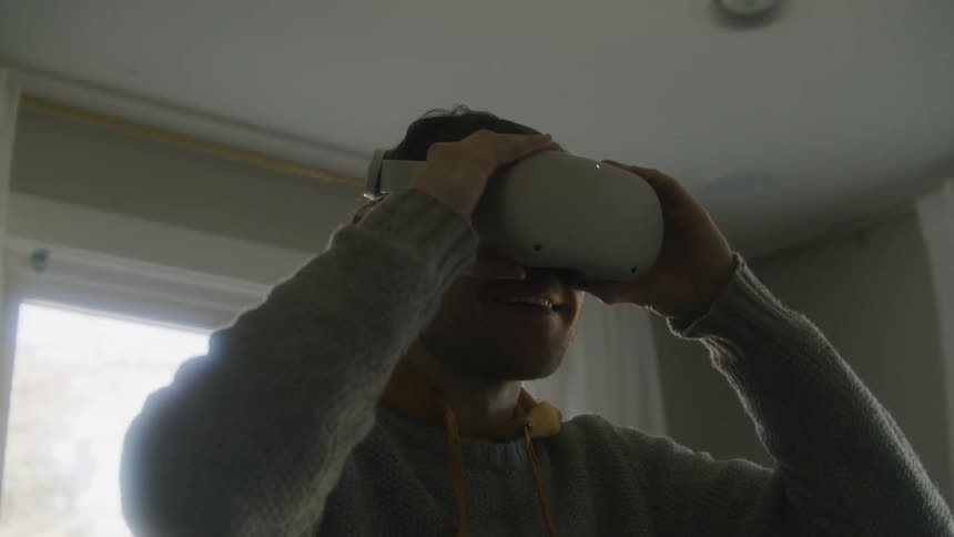 A young man has a smile on his face as he puts on a virtual reality headset