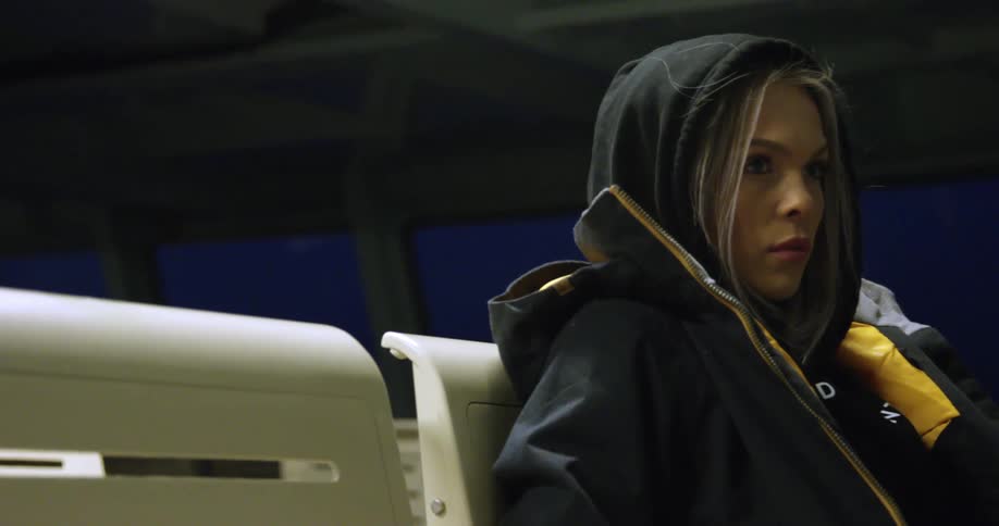 A woman wearing a hoodie and jacket sits in a chair while riding in a ferry