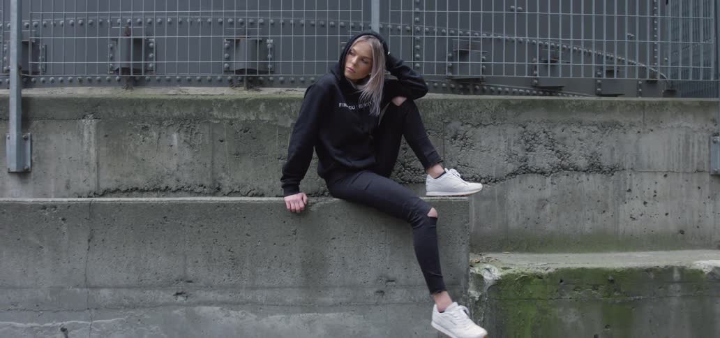 A woman swings her leg while sitting on a ledge next to a road during the day