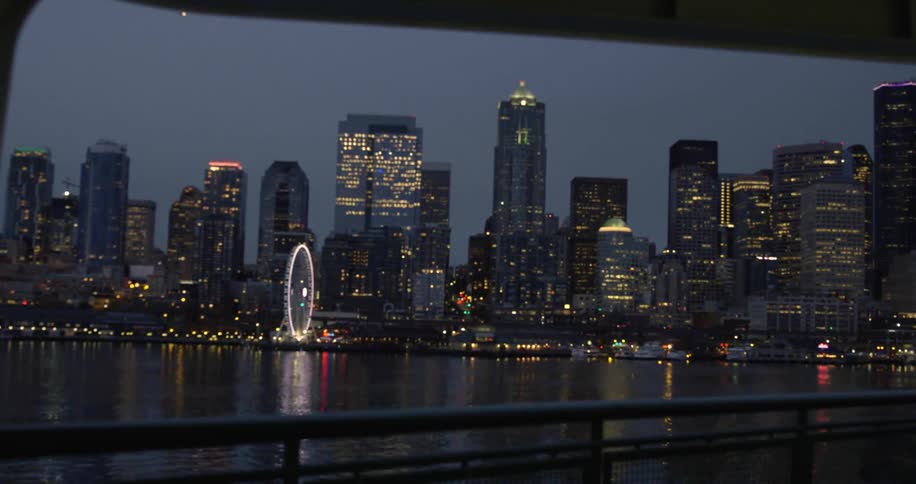 Illuminated skyscrapers and ferris wheel seen from moving boat at night