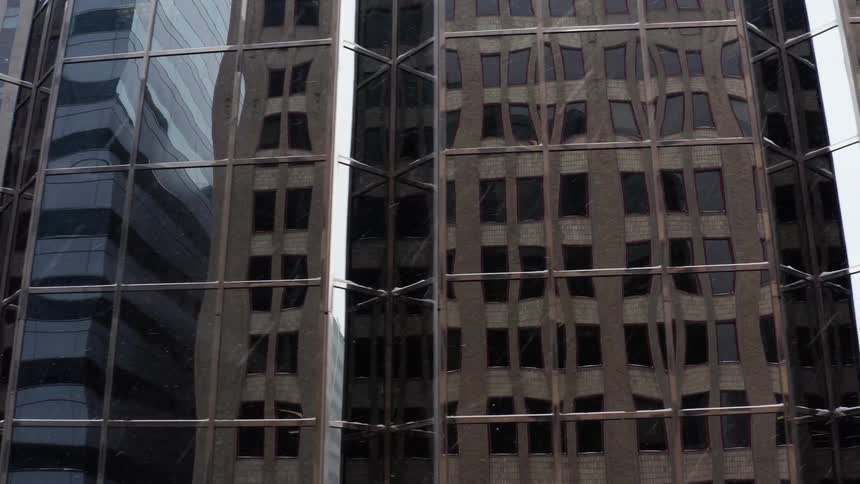 The glass facades of city buildings reflects the surroundings as it starts to snow