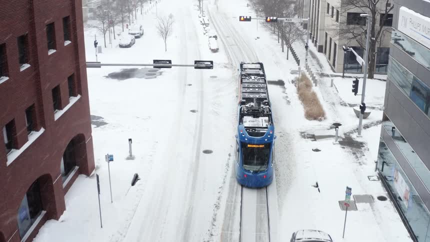 Aerial view tram running on rails along the streets of city while snowing