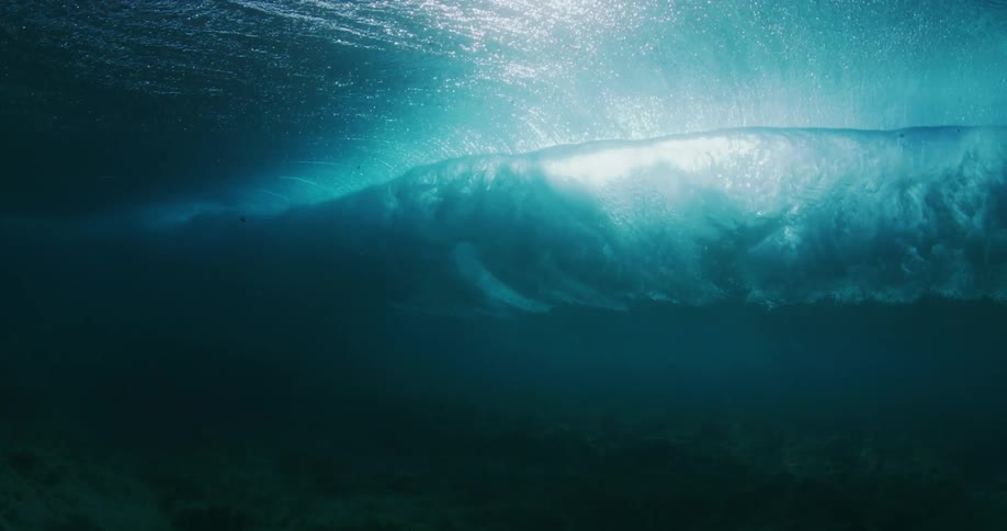 Sunlight shines through the ocean water as waves build and crash