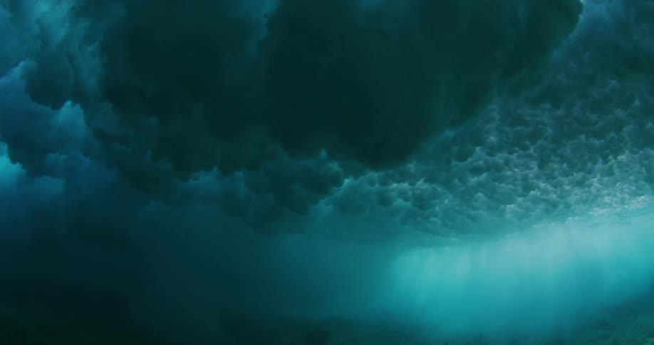 A powerful wave passes overhead and is seen from underneath the surface of the ocean
