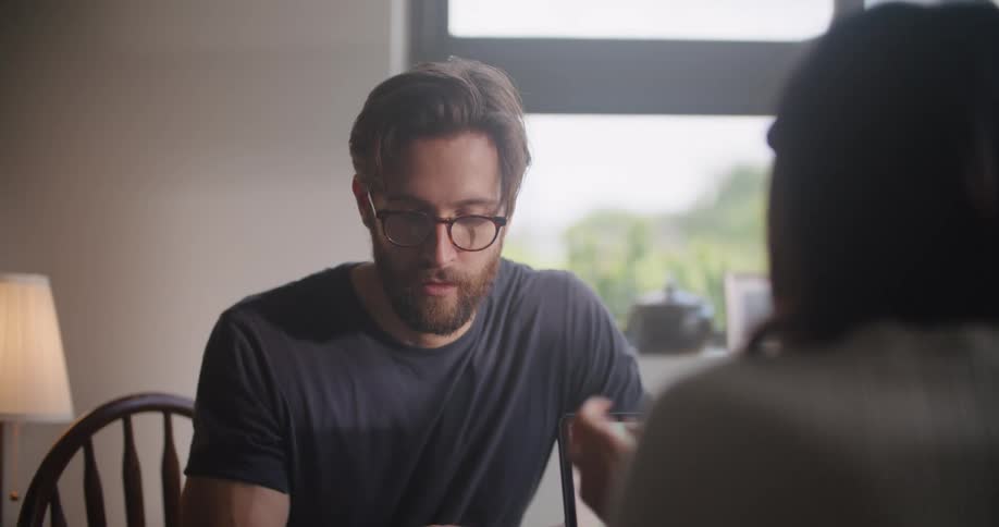 Man and woman sitting at the table indoors talking and using their smartphone and laptop