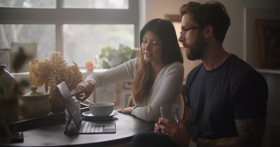 A young woman teaches her partner about something on a tablet
