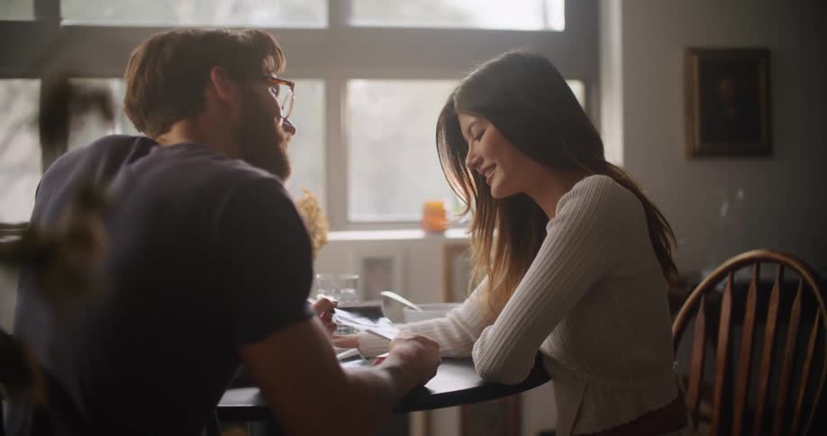 Man and woman sitting at the table indoors talking smiling and gently kissing