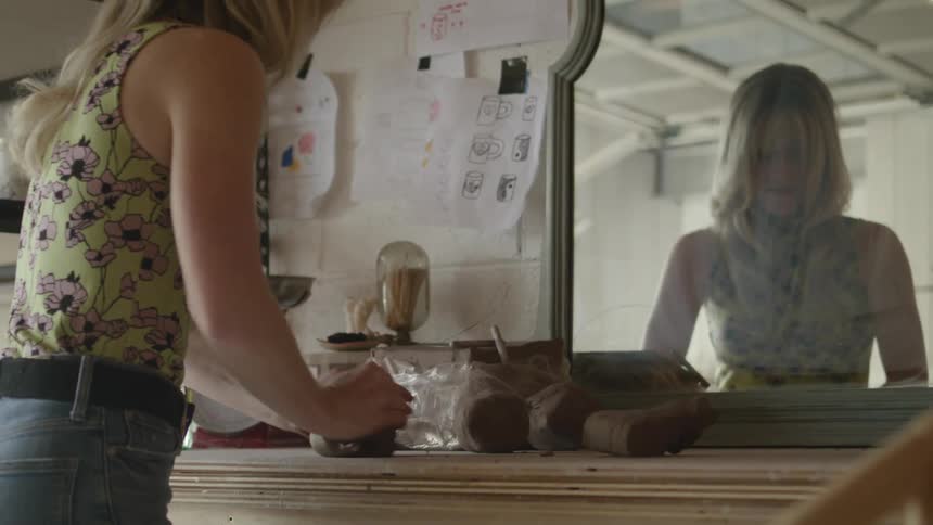 A woman kneading clay on a tabletop in front of a mirror