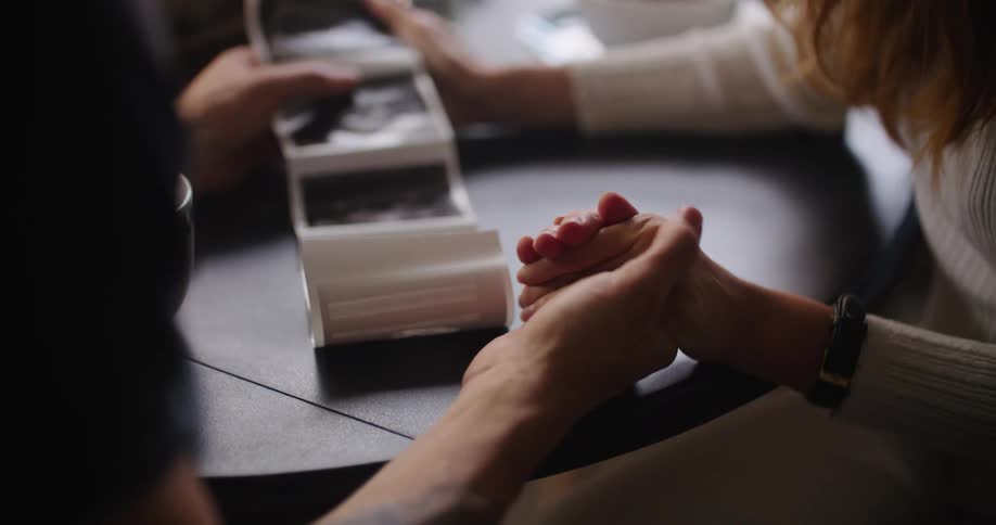 Couple sitting at a table holding hands viewing sonogram images
