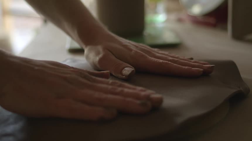 A sculptor pats and smooths clay on a table