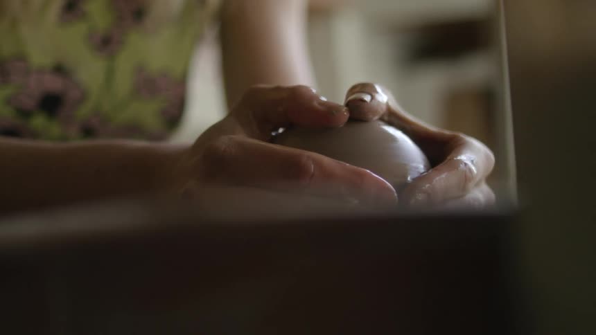 A woman working with clay on a pottery wheel puts water on the clay