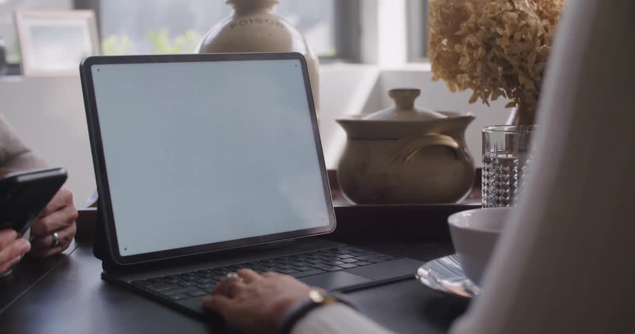 Hand of a woman next to a laptop at the desk with a man using his smartphone next to her