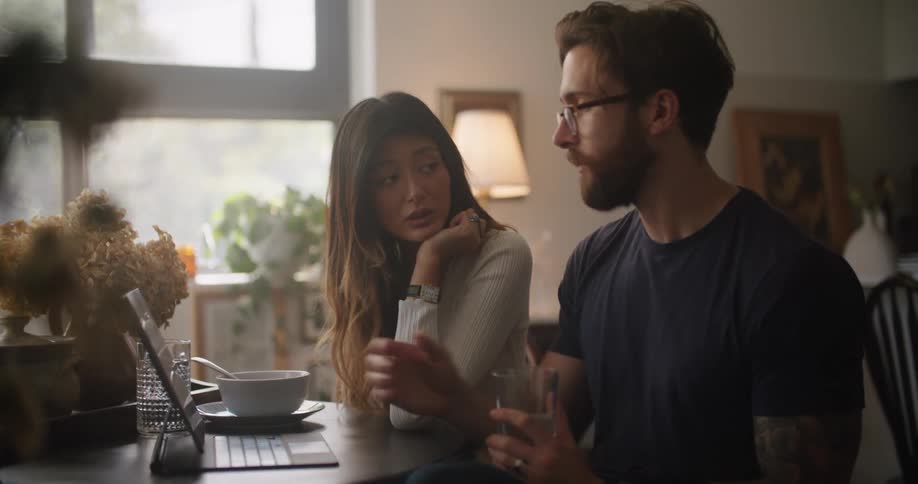 Man and woman sitting together at the table and talking while looking at the laptop