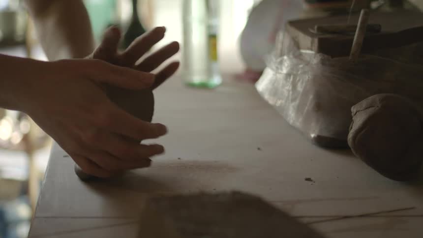A sculptor kneads clay on a table indoors during the day