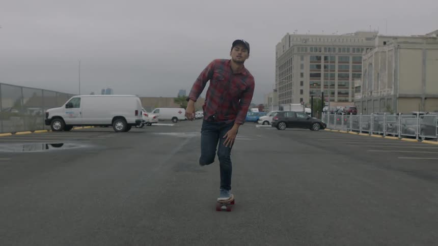 A man is skateboarding down a parking lot