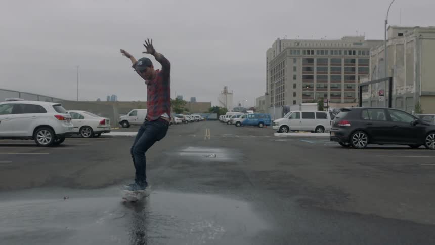 A man skateboards right through a puddle