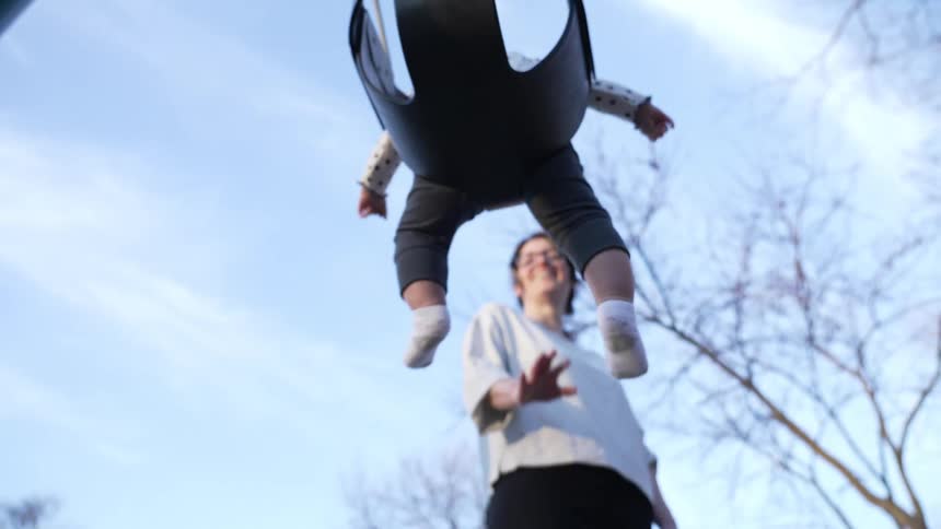 A woman pushes a baby on a swing outdoors on a sunny day
