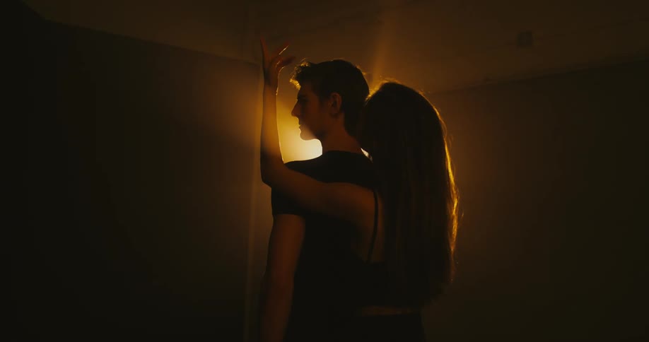 A woman stands behind a man and rubs her hand on his back and over his head and then leans over his shoulder to look at him
