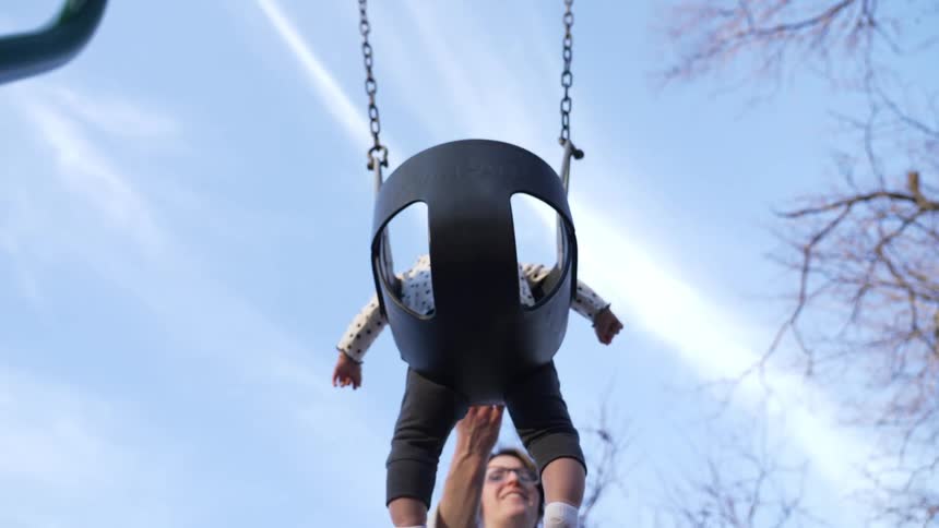 A woman pushes her baby in a swing at a playground