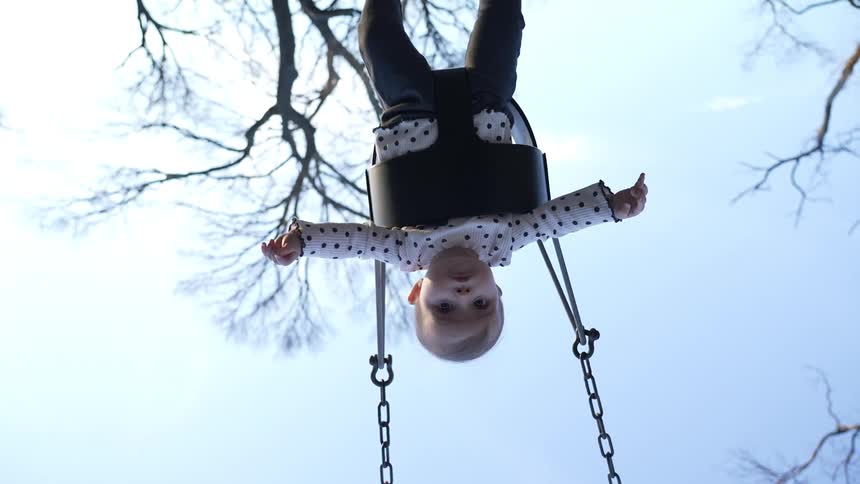 A woman pushes a baby on a swing set outdoors on a sunny day