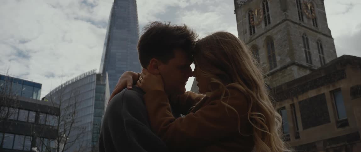 A couple kiss while standing near tall skyscrapers downtown