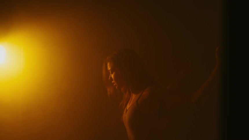 Female dancer moves through dance in dark shadowy room lit by amber spotlight