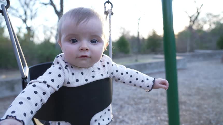 Baby having fun sitting on a fullbucket baby swing at an outdoors playground