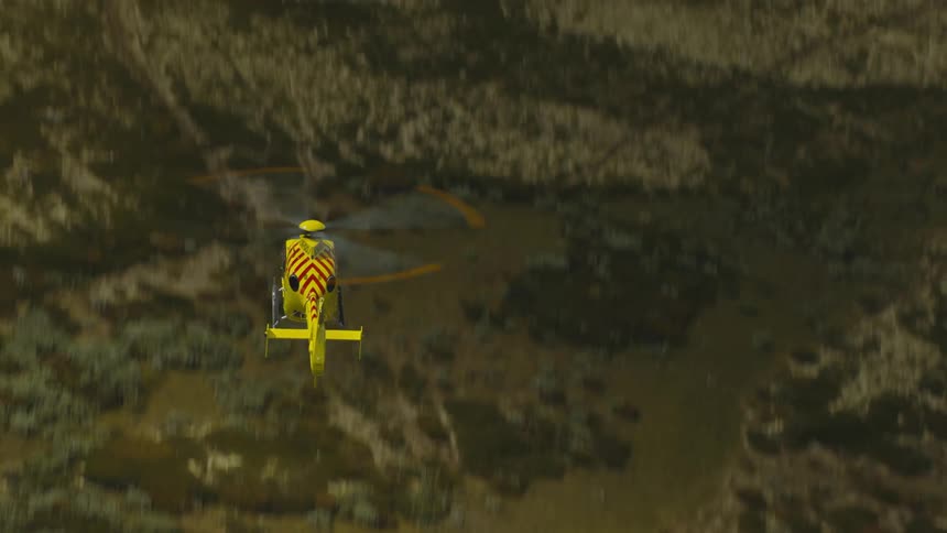 View from above of a yellow and red rescue helicopter flying over land and trees