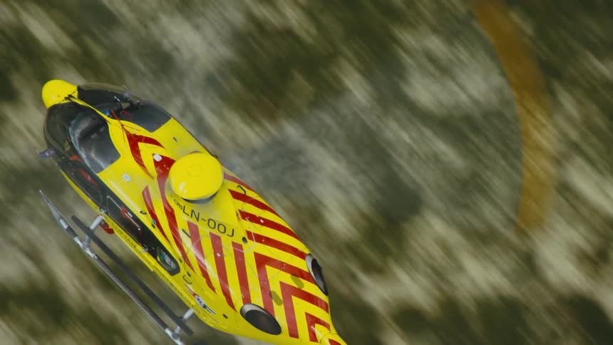 View from above of a yellow and red rescue helicopter flying over land