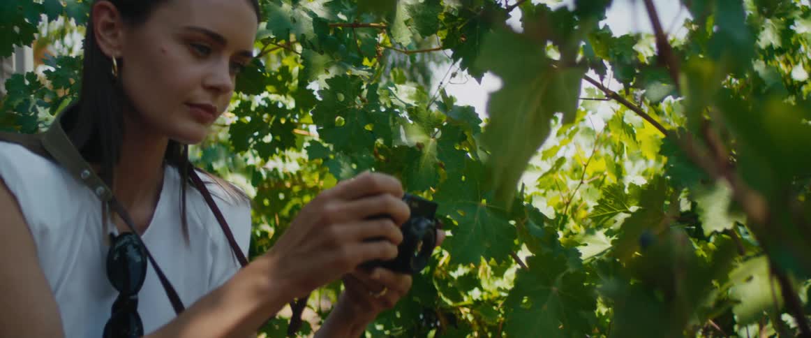 Woman takes pictures of grapes on plants planted near building