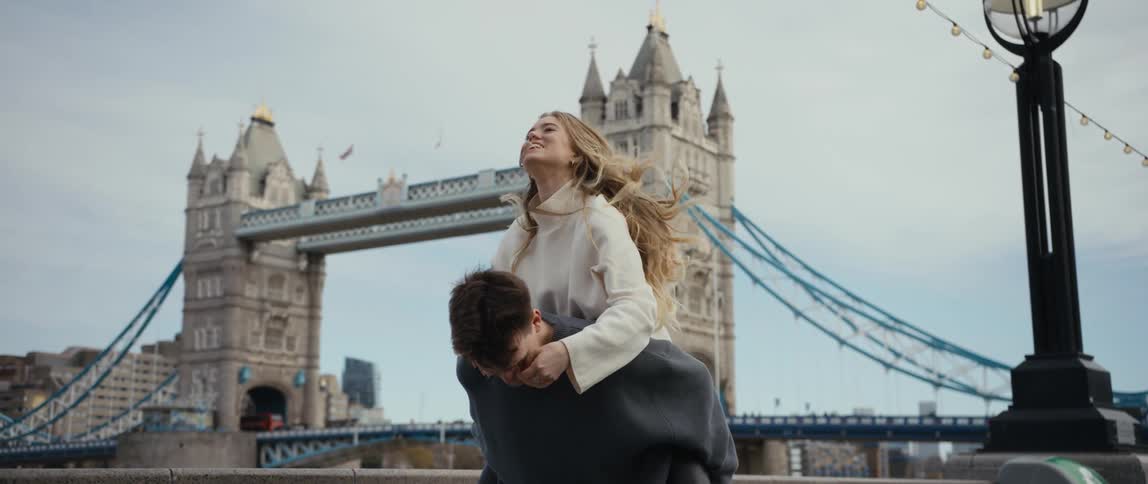 A woman hops on her boyfriends back for a piggyback ride as they walk past a bridge