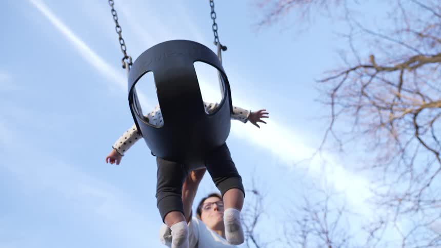 Mother swings baby in swing in playground at sunset