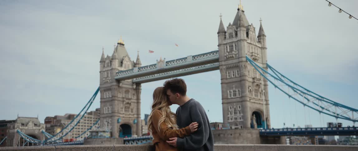 Man and woman kissing and hugging each other at a public space in front of a famous bridge