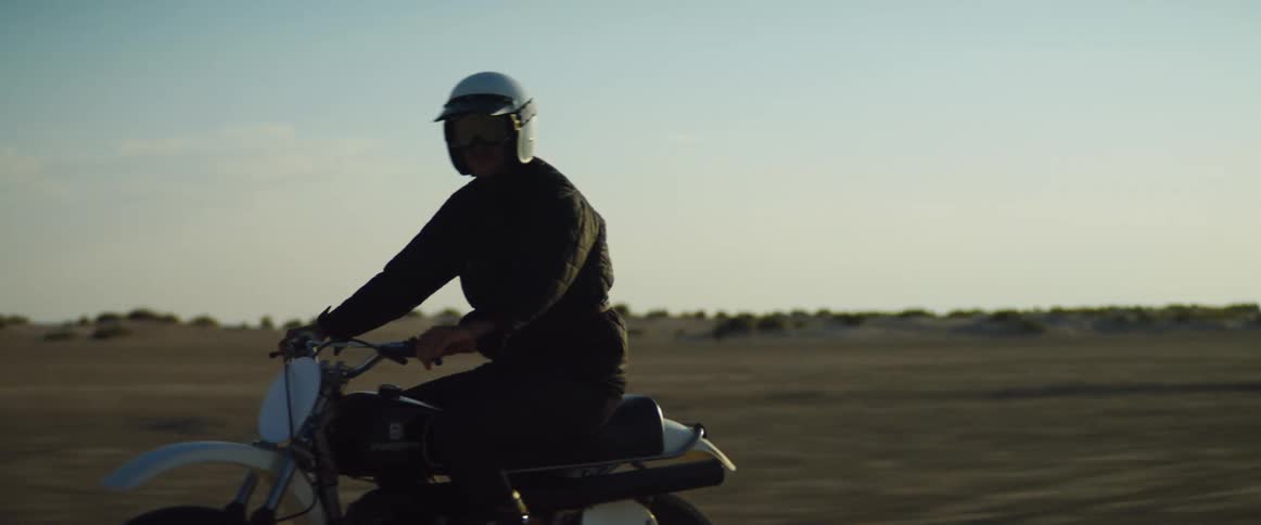 A man wearing a white helmet drives his dirt bike atop a dusty desert plain