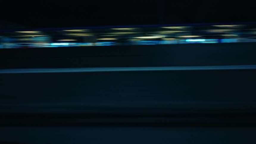 Vehicle casts shadow as it moves along highway passing brightly lit overpass bridge and buildings