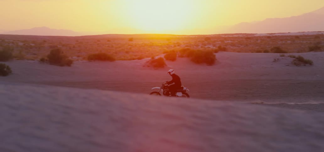 A man wearing a white helmet can be seen as he drives his motorcycle around a desert landscape