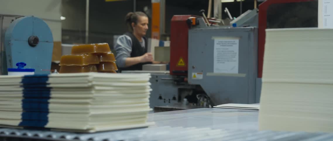 A woman feeds paper into a machine at a factory