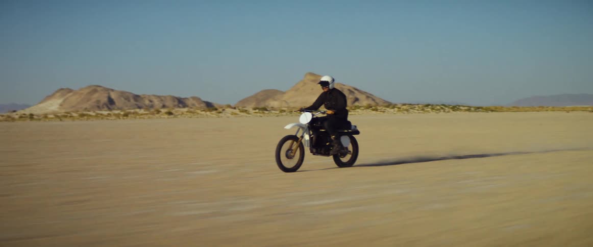 A person rides a motorcycle through an arid flatland during the day