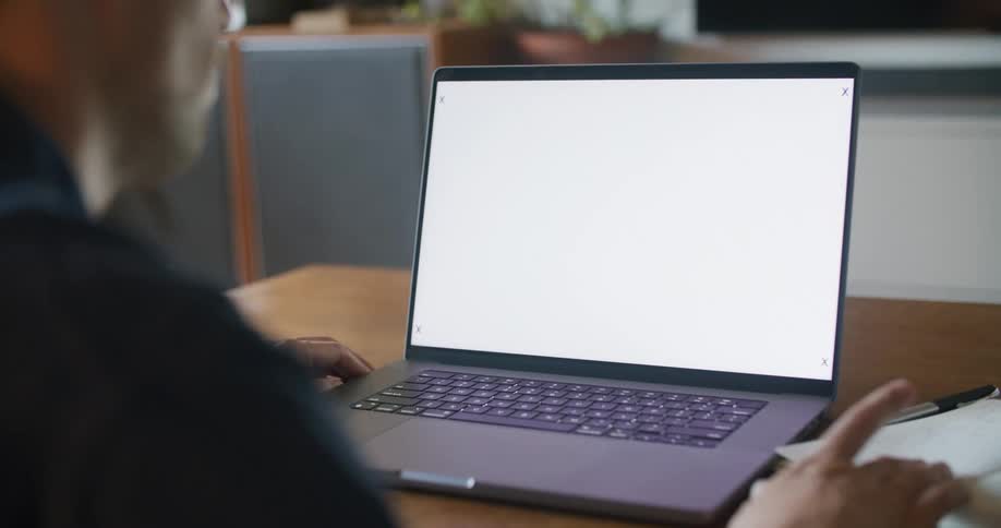 Man sits in front of laptop comparing notes to computer screen