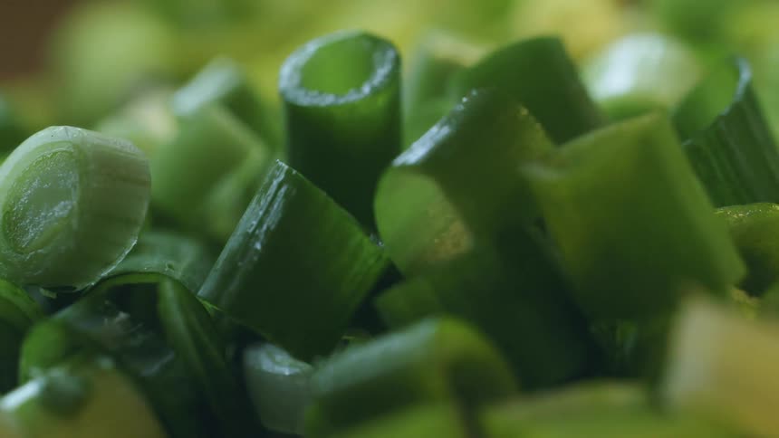 A hand touching a pile of chopped green onion
