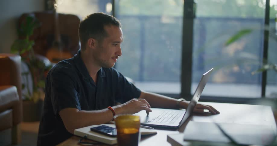 Man with mustache and blue shirt opens and works laptop at coffee table