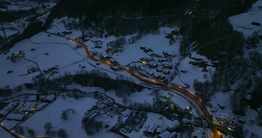 A road through a small town in a snowy countryside at night