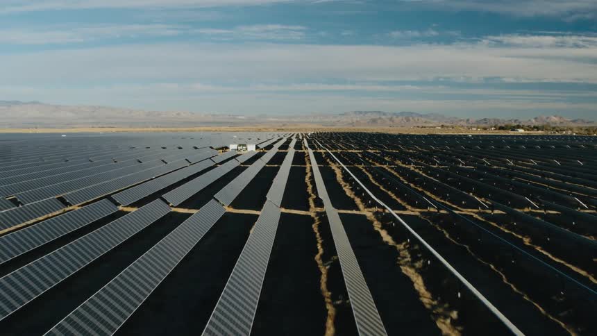 Sunlight shines on solar panels on a solar farm with mountains in the distance
