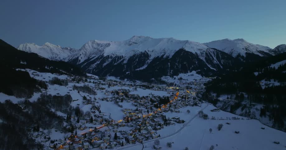 Aerial view of snowy town in valley surrounded by snowy mountains at dusk