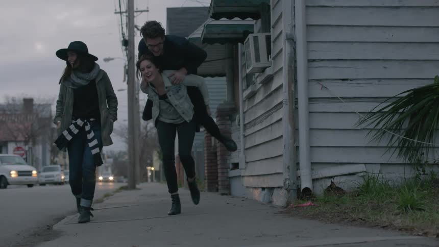 People walk down a sidewalk one gives a piggyback ride to a friend