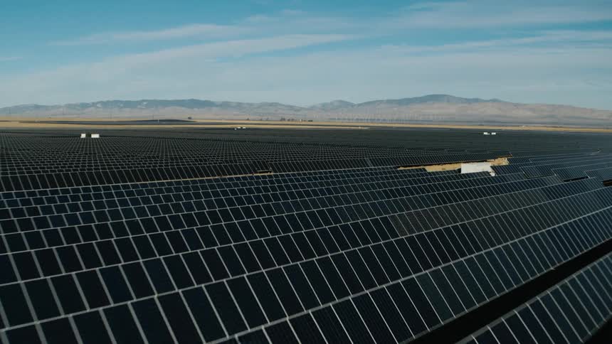 Sunlight shines on solar panels on a solar farm with mountains in the distance