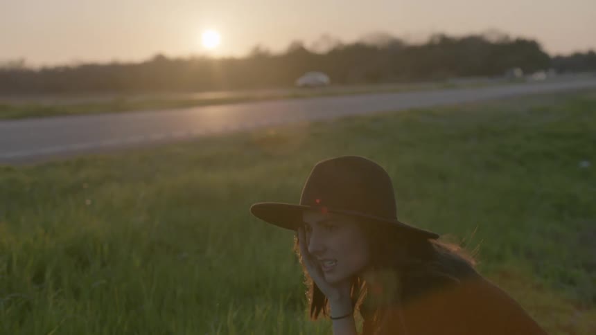 A woman is crouching in a field of grass at sunset