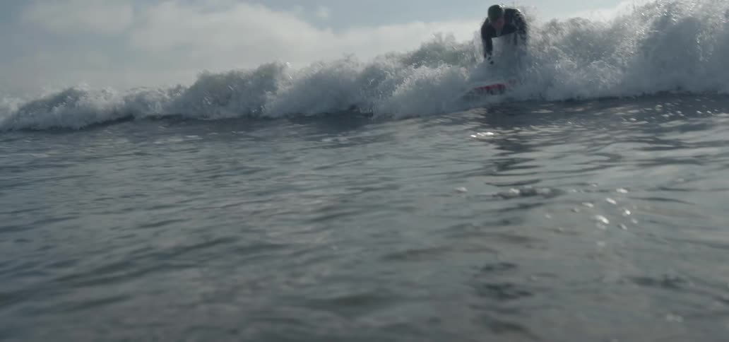 Man wearing a male wetsuit surfing a wave at a sunny day